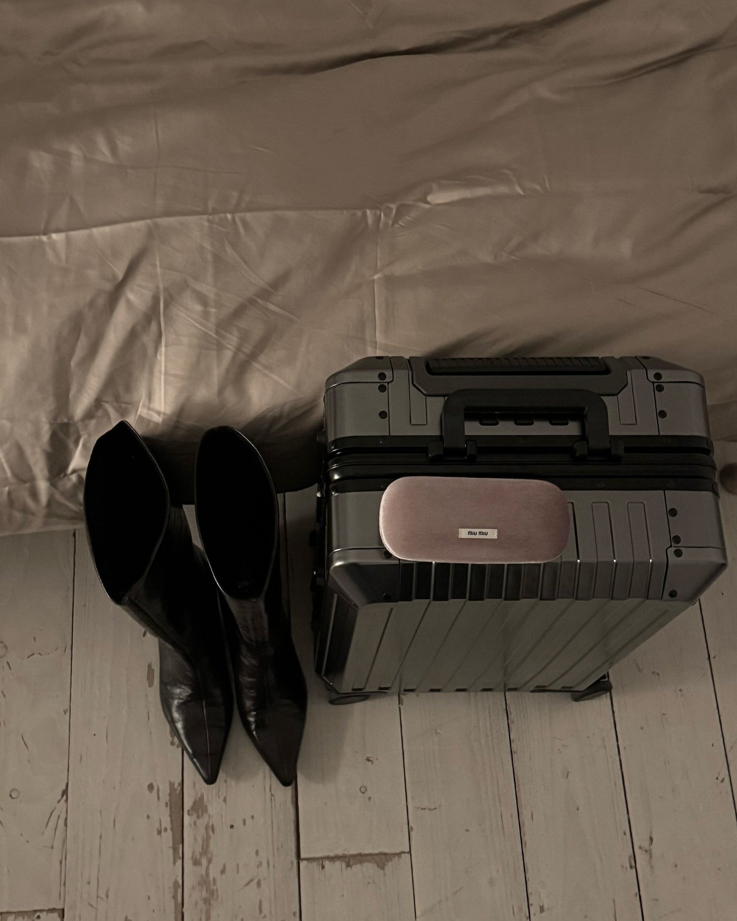 Black aluminum suitcase with a sleek hard shell, sturdy handle, and minimalist design, paired with black leather boots, perfect for luxury and business travel.