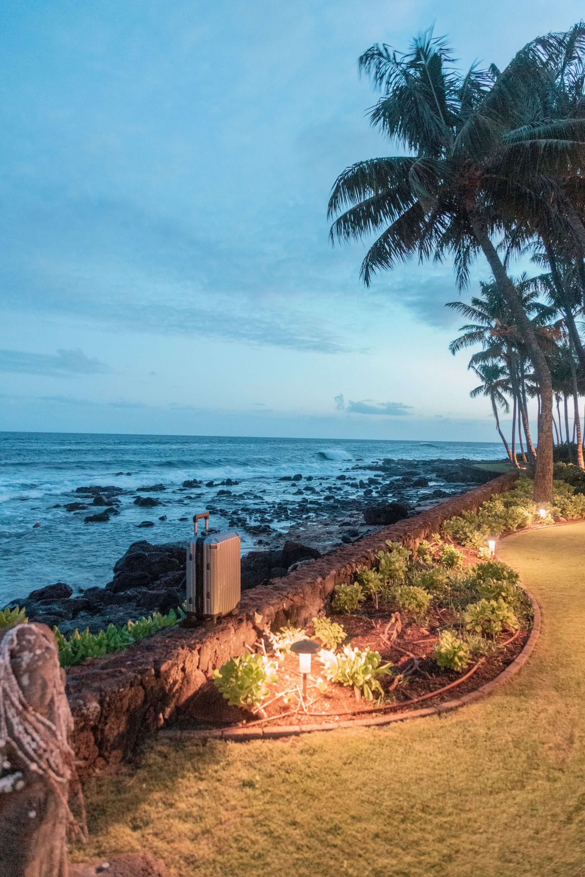 Silver aluminum suitcase with a sleek modern design, standing against a scenic beach view at sunset, perfect for luxury travel